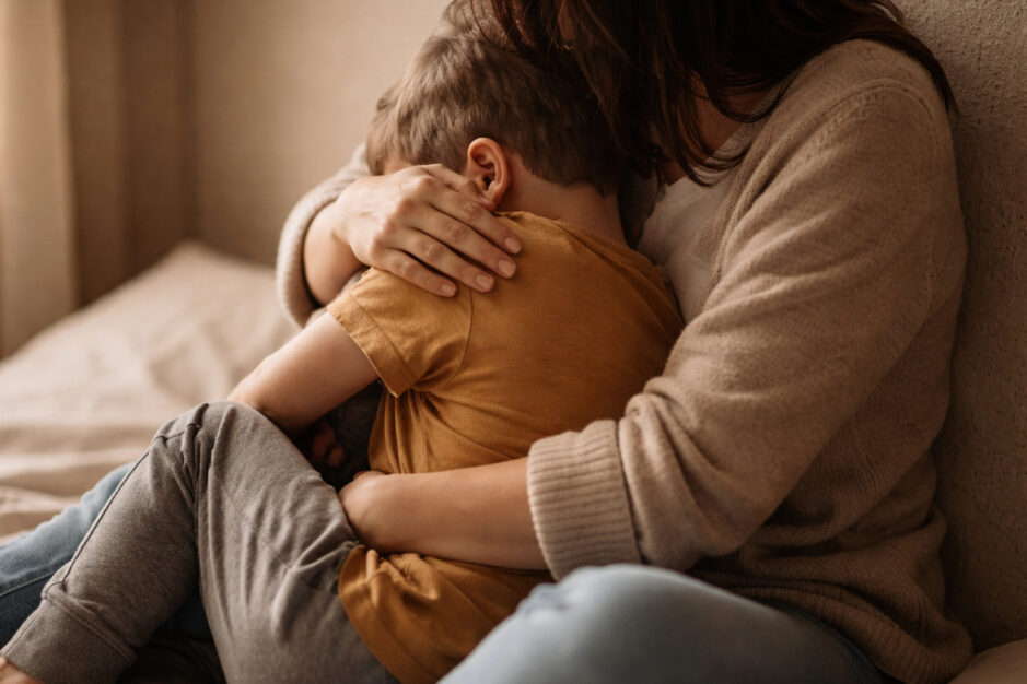 Mamma che abbraccia il figlio seduti sul letto.