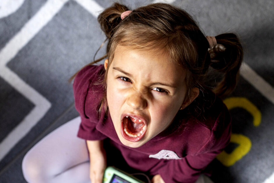 Bambina seduta su di un tappeto che guarda all'insù e urla.