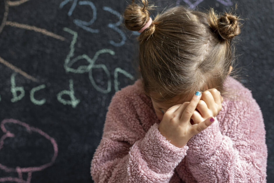 bambina davanti ad una lavagna che si copre il volto