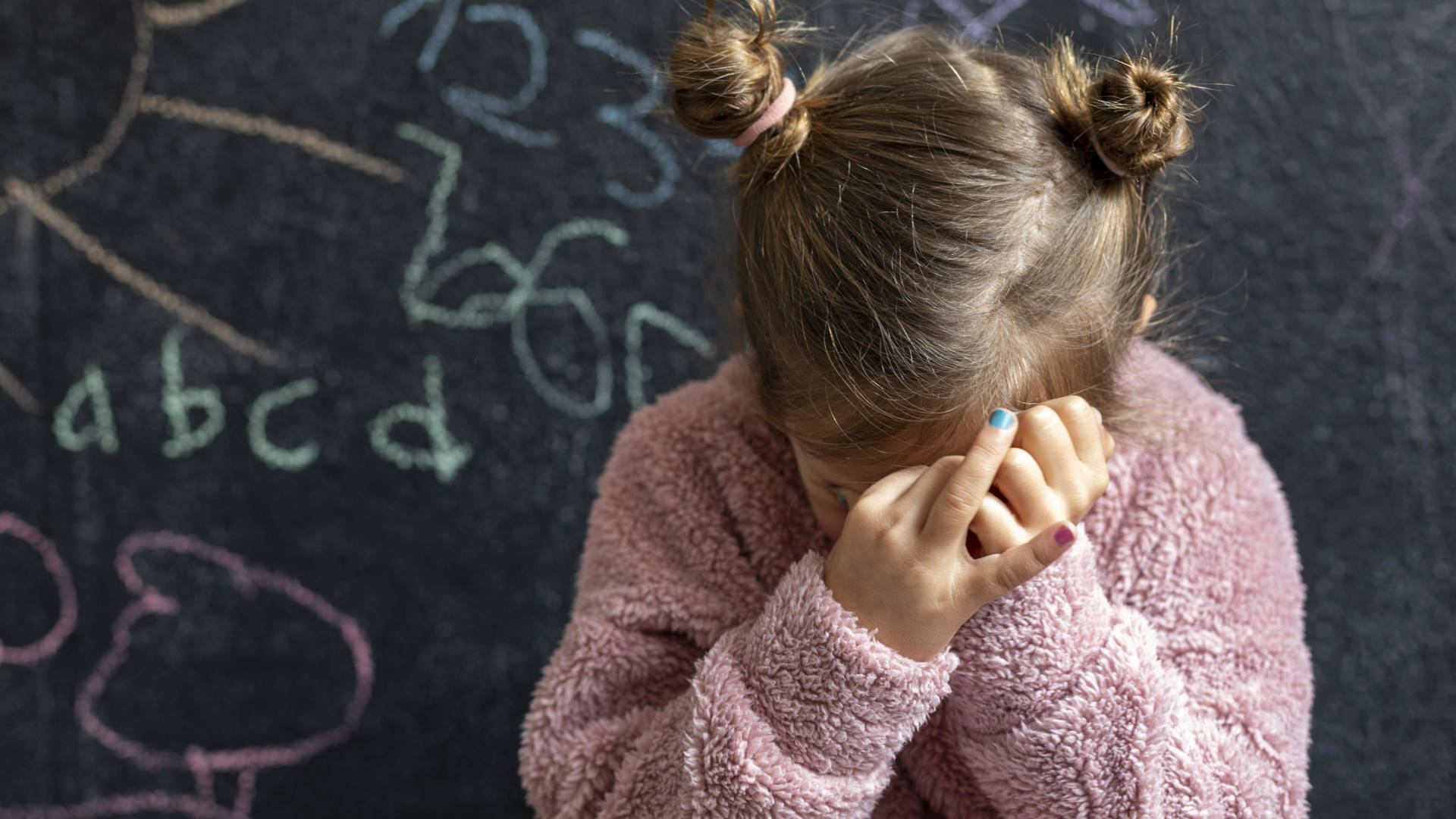 bambina davanti ad una lavagna che si copre il volto