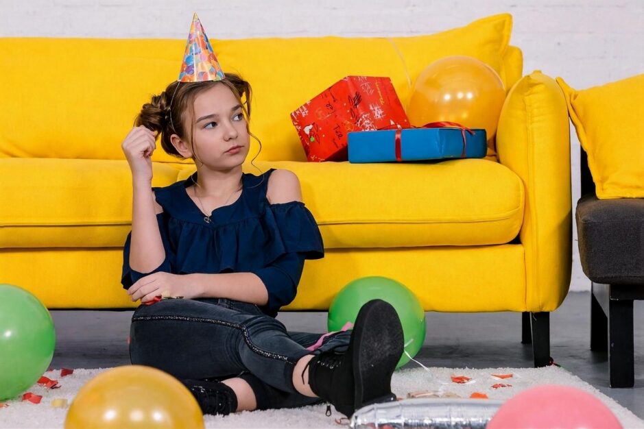 Bambina seduta davanti al divano il giorno del suo compleanno con sguardo arrabbiato