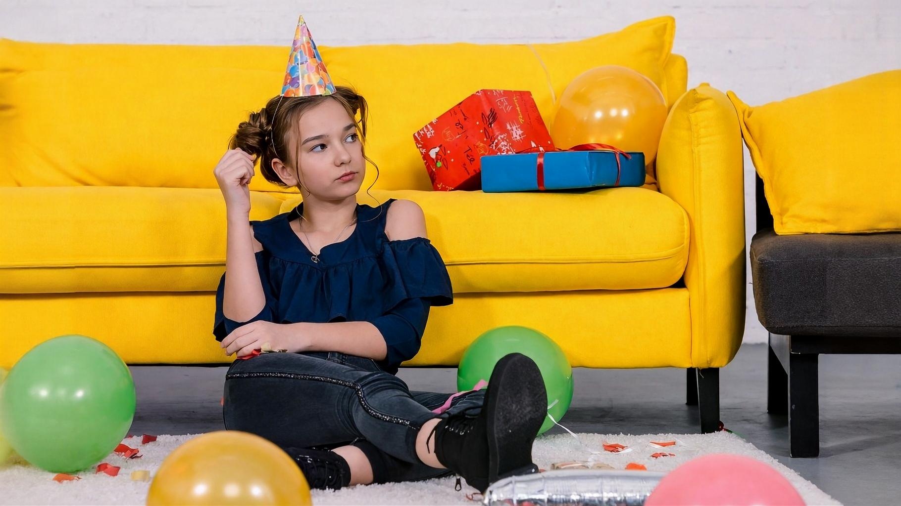 Bambina seduta davanti al divano il giorno del suo compleanno con sguardo arrabbiato