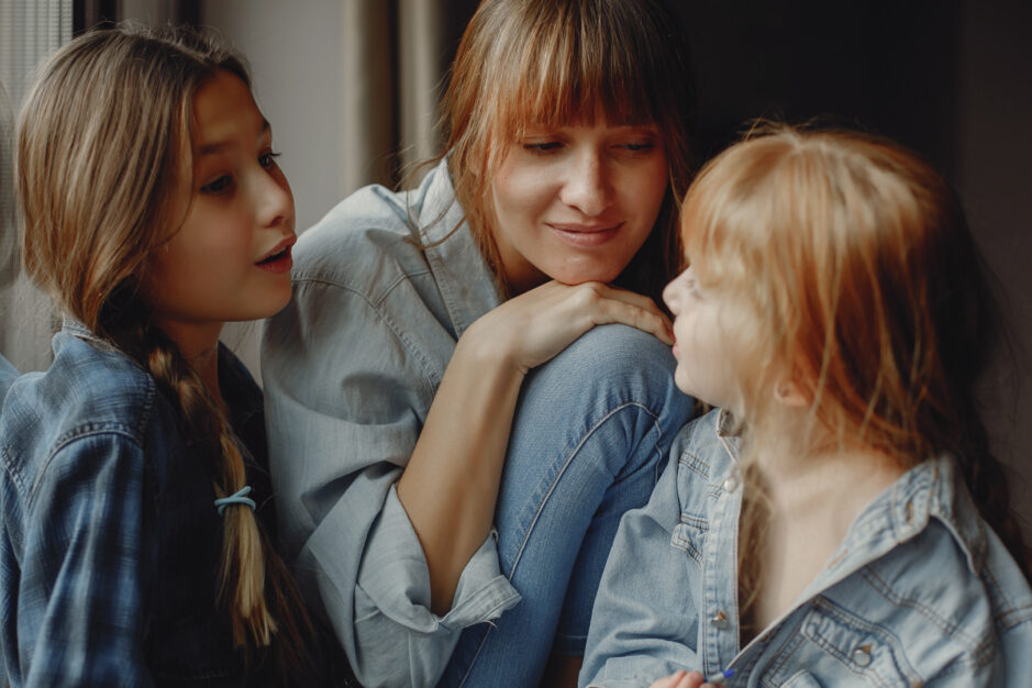 Mamma accovacciata con due figlie a conversare con volto dolce e interessato.