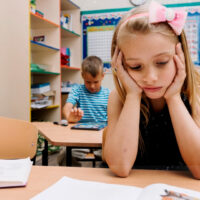 Bambina al banco di scuola annoiata